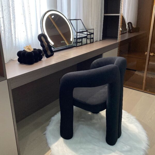 Black modern upholstered accent chair with a curved backrest and cylindrical legs in a minimal interior setting.