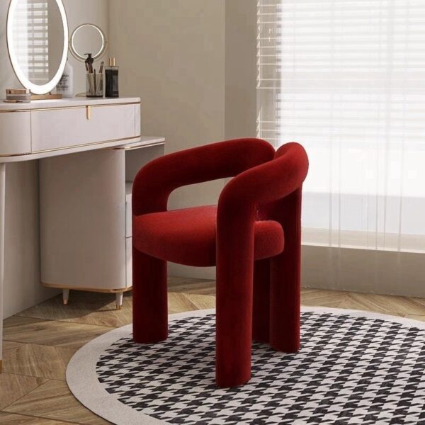 Red modern upholstered accent chair with a curved backrest and cylindrical legs in a minimalist room.