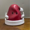 Red Liver-Shaped Anthropomorphic Decorative Ornament (With White Hands) on White Base, Placed on Wooden Surface
