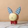 An ins-style decorative ornament featuring a hand-drawn cartoon pet with blue striped big ears, a round yellow face with a mischievous grin, a textured brown body, and red segmented legs, crafted from resin. Displayed on a marble countertop against a peach backdrop, it adds a playful, quirky charm to kids' rooms, desks, or modern living spaces.