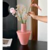 Pastel Pink Decorative Vase – Stylish Floral Accent for Home Interiors A modern minimalist bright pink glass vase with a tapered silhouette and tall narrow neck, displayed on a black tabletop while being arranged with pink iris, baby's breath, and calla lily. The sleek, glossy finish contrasts with the dark cabinet and wooden panel backdrop, adding a vibrant pop of color to the modern space.