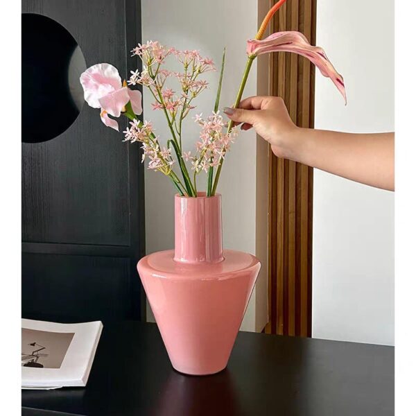 Pastel Pink Decorative Vase – Stylish Floral Accent for Home Interiors A modern minimalist bright pink glass vase with a tapered silhouette and tall narrow neck, displayed on a black tabletop while being arranged with pink iris, baby's breath, and calla lily. The sleek, glossy finish contrasts with the dark cabinet and wooden panel backdrop, adding a vibrant pop of color to the modern space.