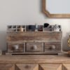 A rustic wooden makeup organizer filled with cosmetics, sitting on a wooden vanity table in a farmhouse style bedroom. A vintage mirror hangs on the wall in the background.