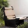 A wabi-sabi style lounge chair with a weather-resistant black solid wood frame and handwoven natural rope upholstery, displayed in an outdoor garden with lush greenery and gravel. It blends rustic texture with minimalist design, ideal for serene outdoor relaxation spaces.