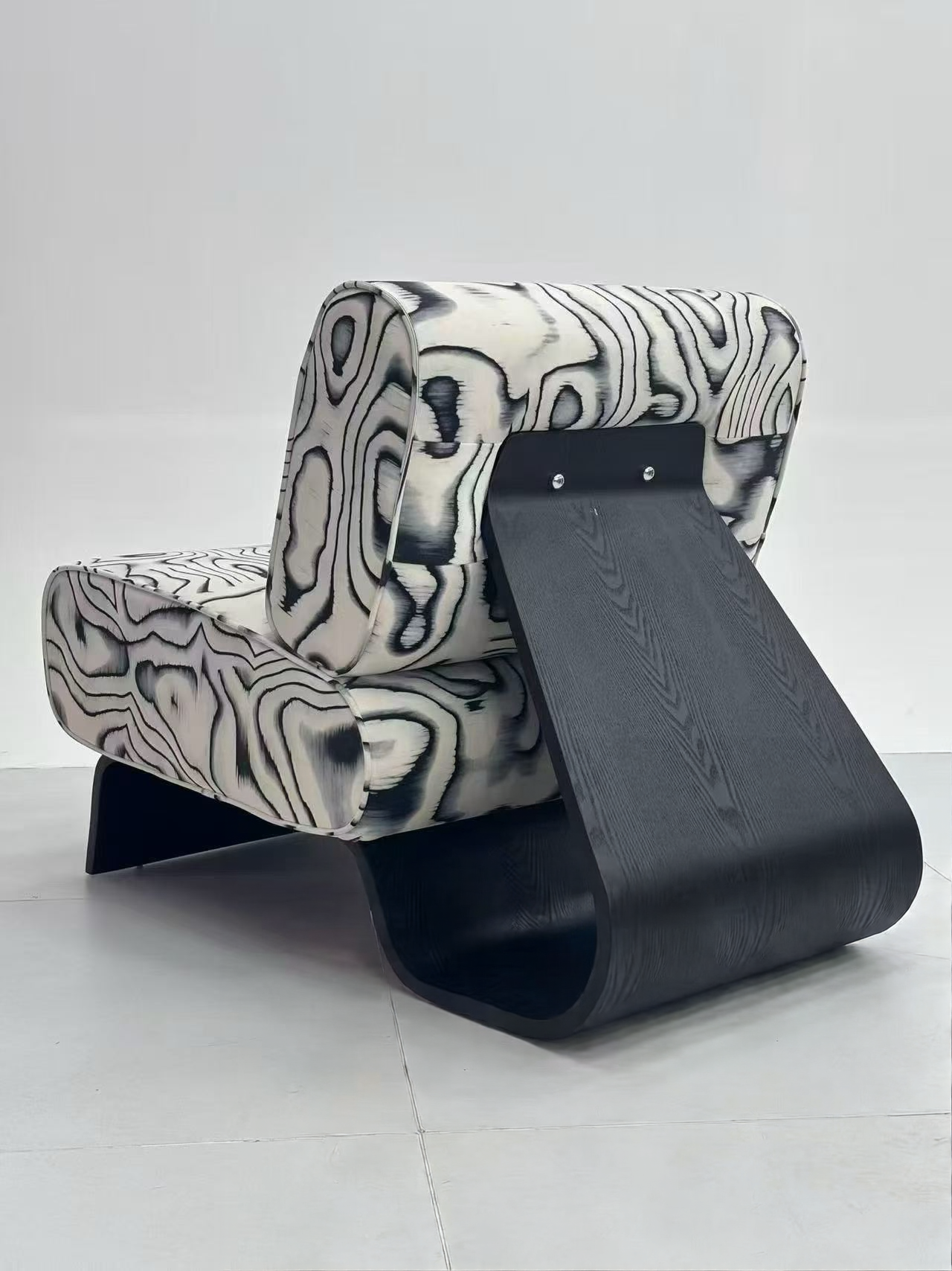 Sculptural slipper accent chair in black and white swirl pattern upholstery with curved black bentwood base, rear three-quarter view