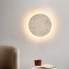 Round travertine LED wall lamp glowing on a beige wall above a sofa in a wabi-sabi living room